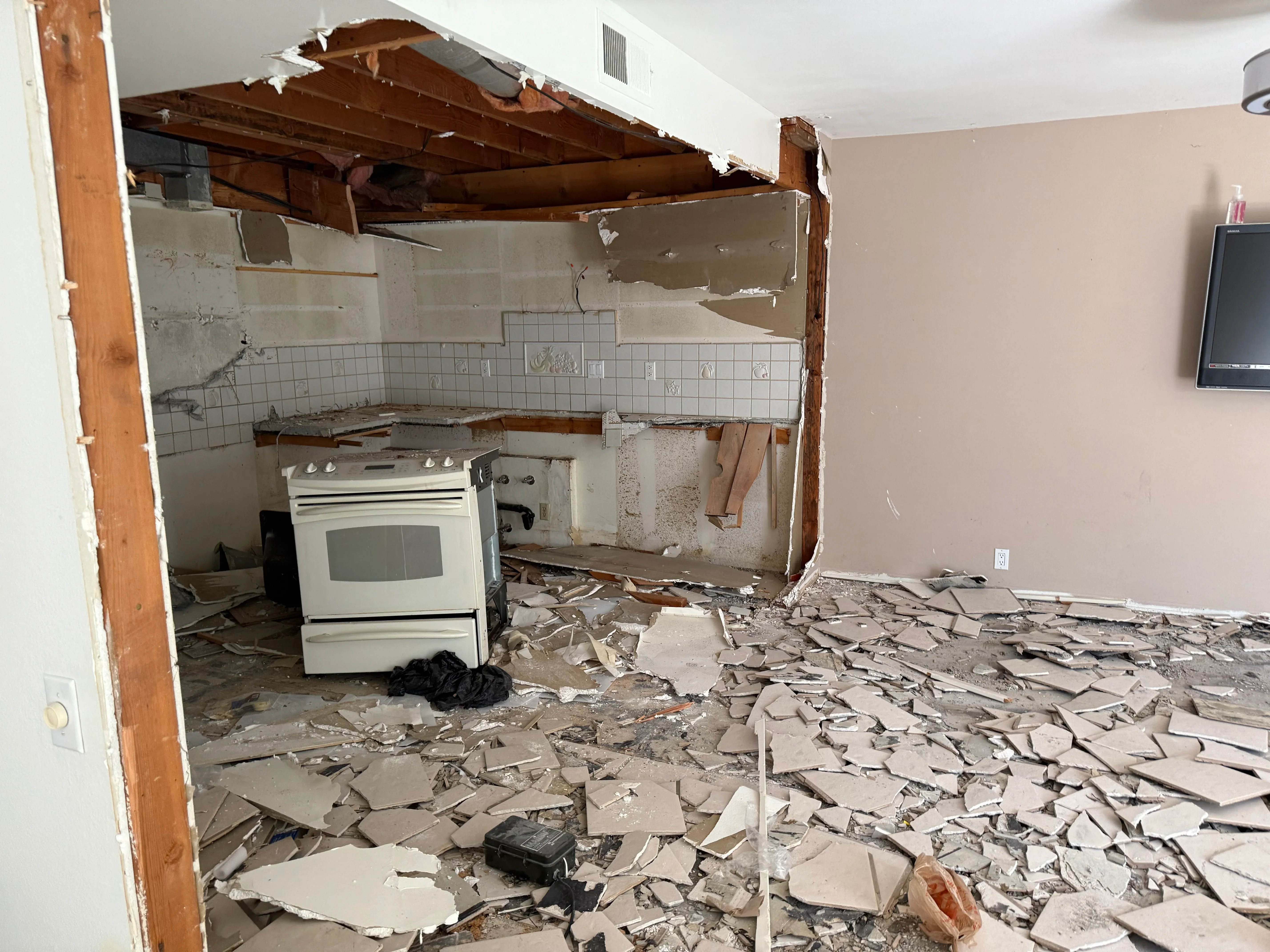 Kitchen demolition showing exposed framing, removed drywall, tile backsplash, and debris cleanup