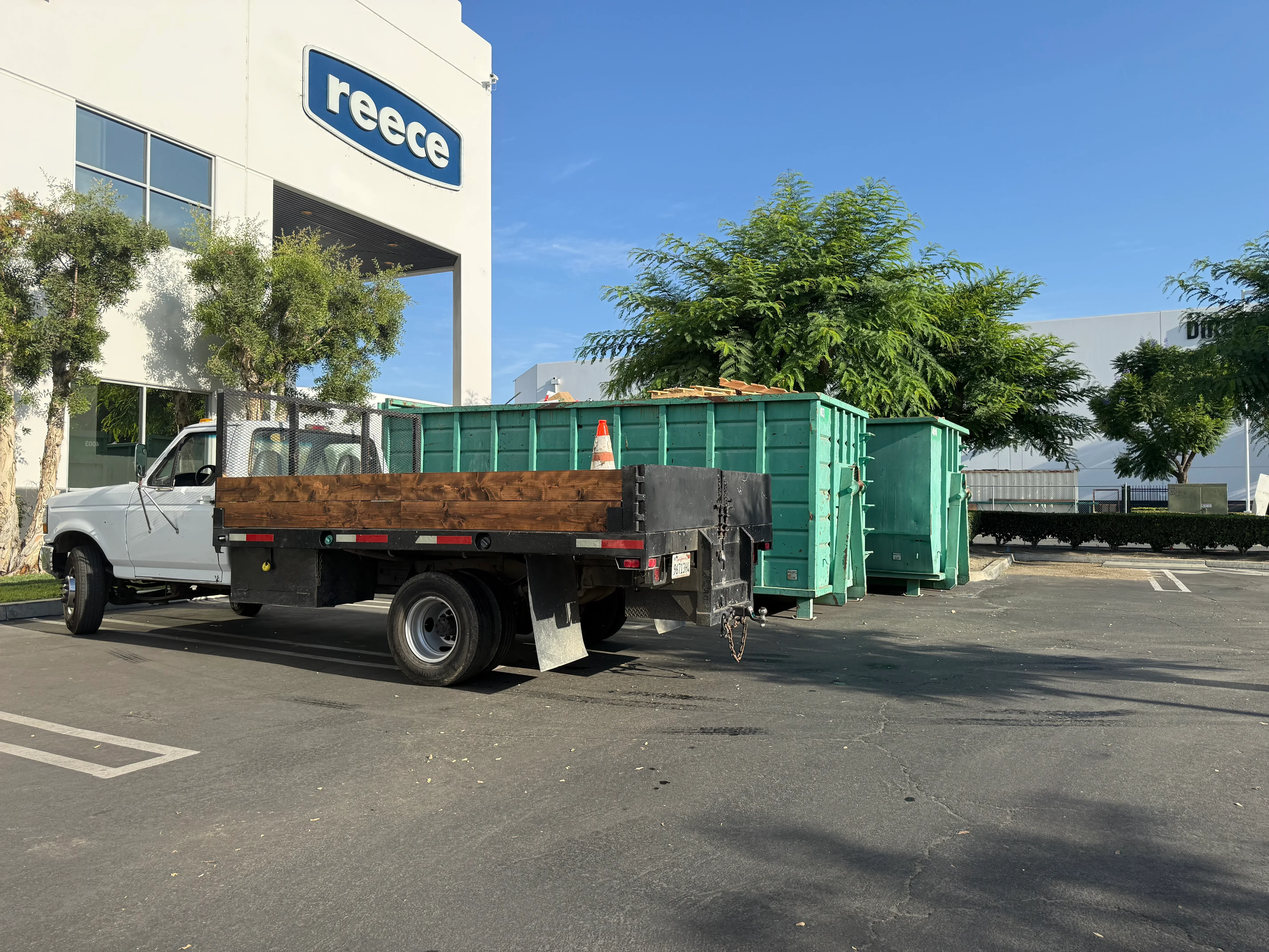 White flatbed truck with wooden sides and green enclosed trailer loaded with construction debris