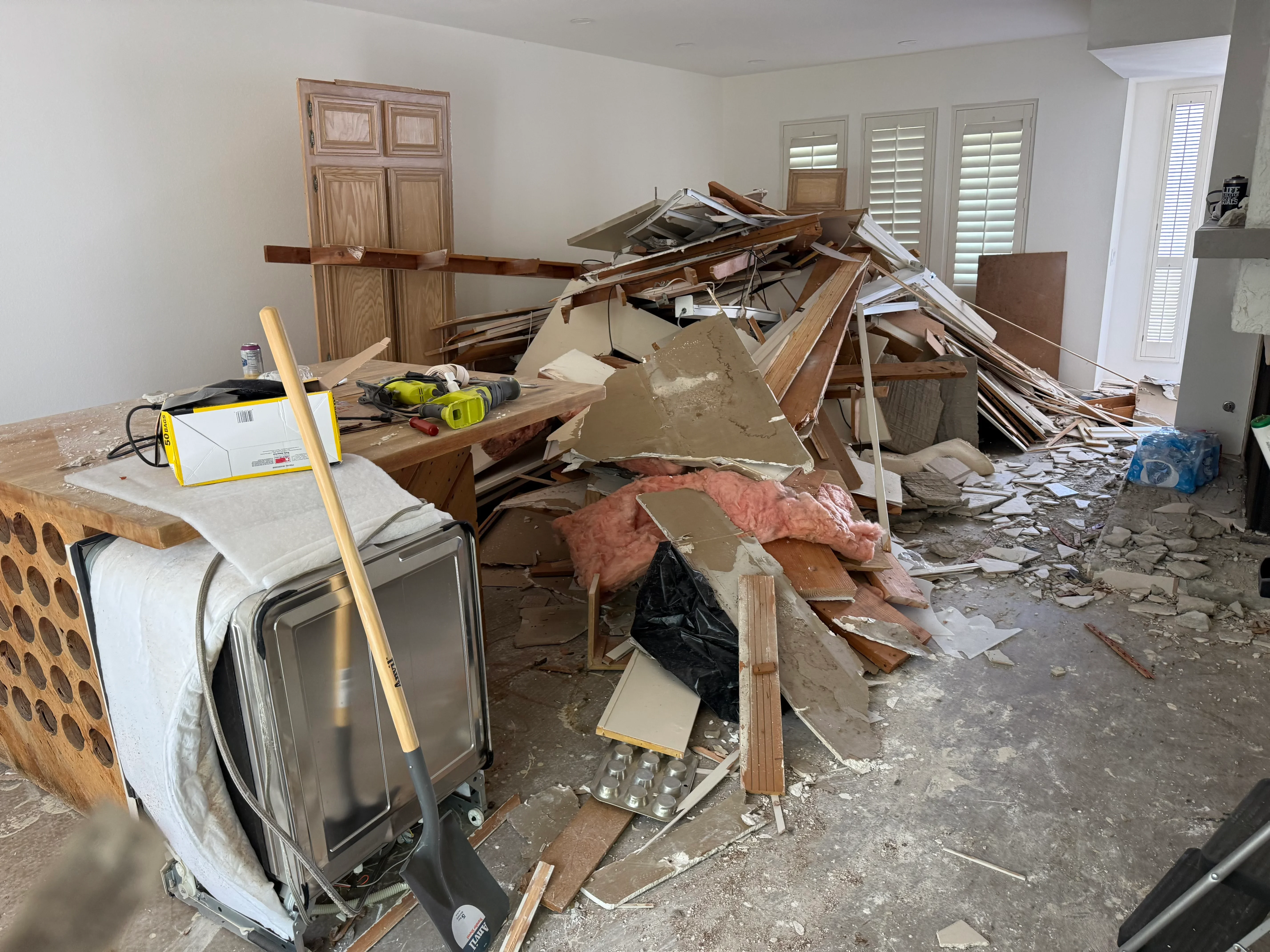 Interior demolition with exposed framing, removed cabinetry, drywall, and debris pile ready for removal