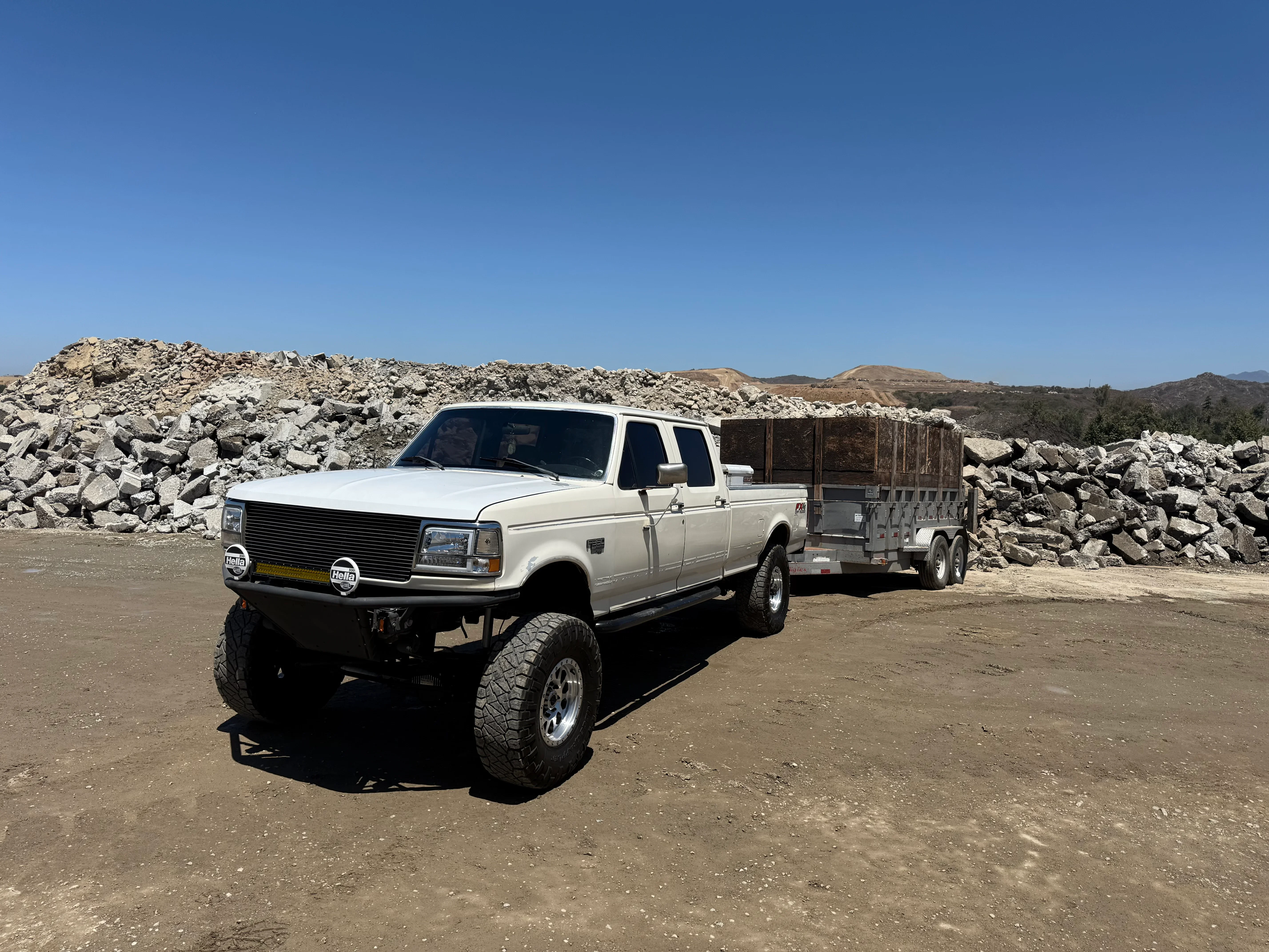 White pickup truck with dual-axle trailer loaded with concrete rubble and debris at demolition site