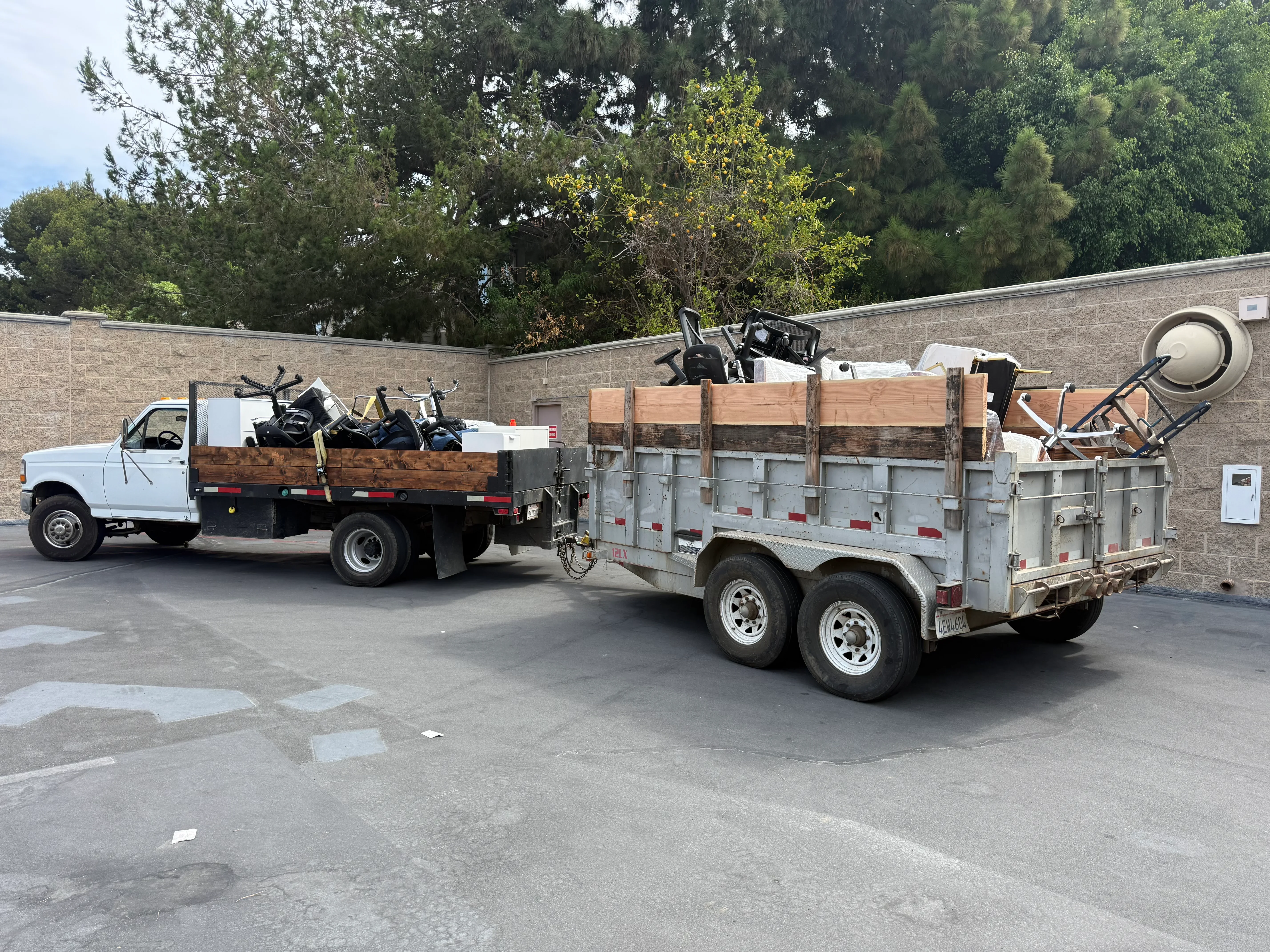 Flatbed truck and dual-axle trailer loaded with construction debris, appliances, and mixed junk materials