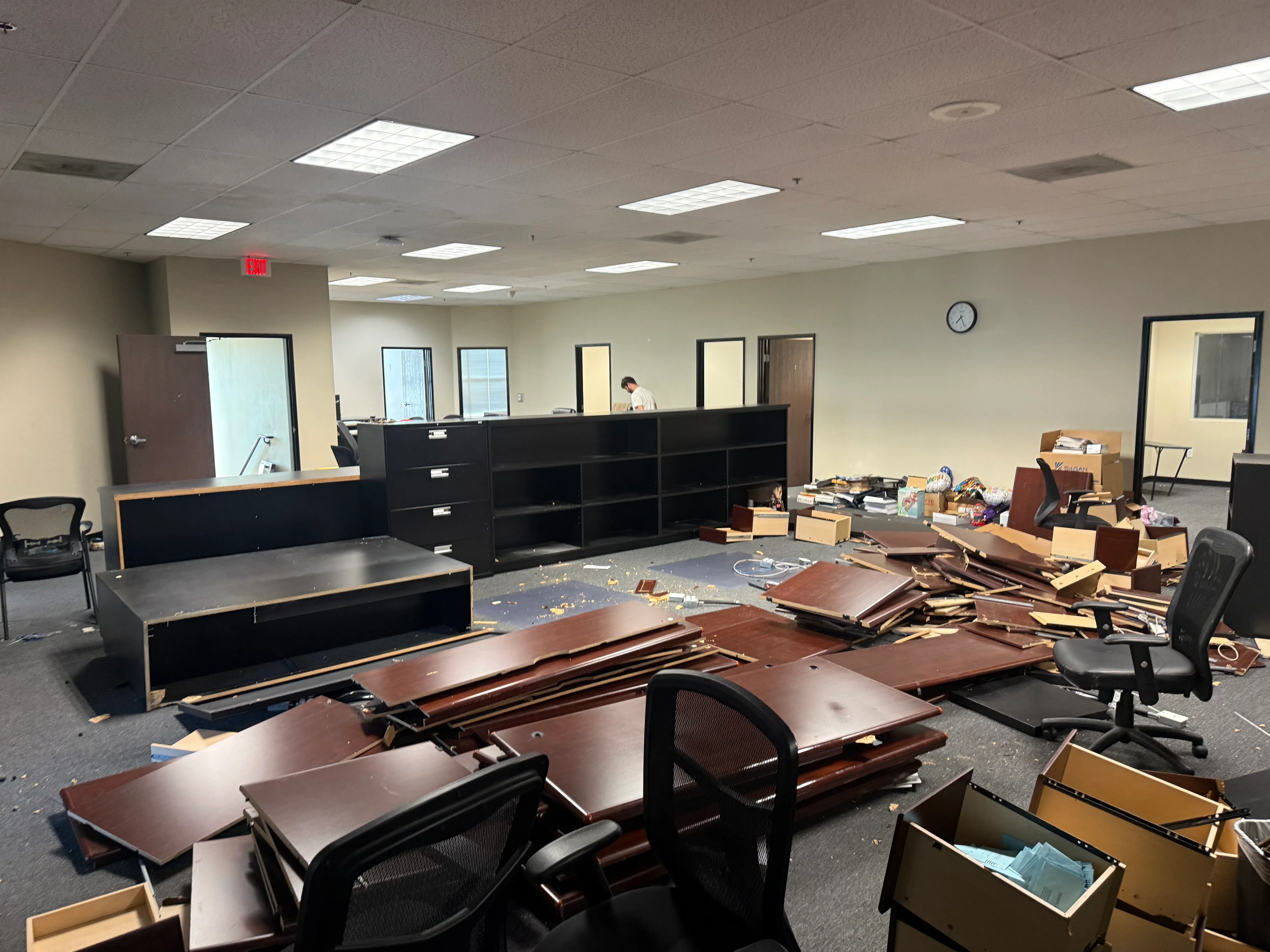 Commercial office interior with dismantled furniture, wooden desks, black cabinetry, and cardboard boxes staged for removal