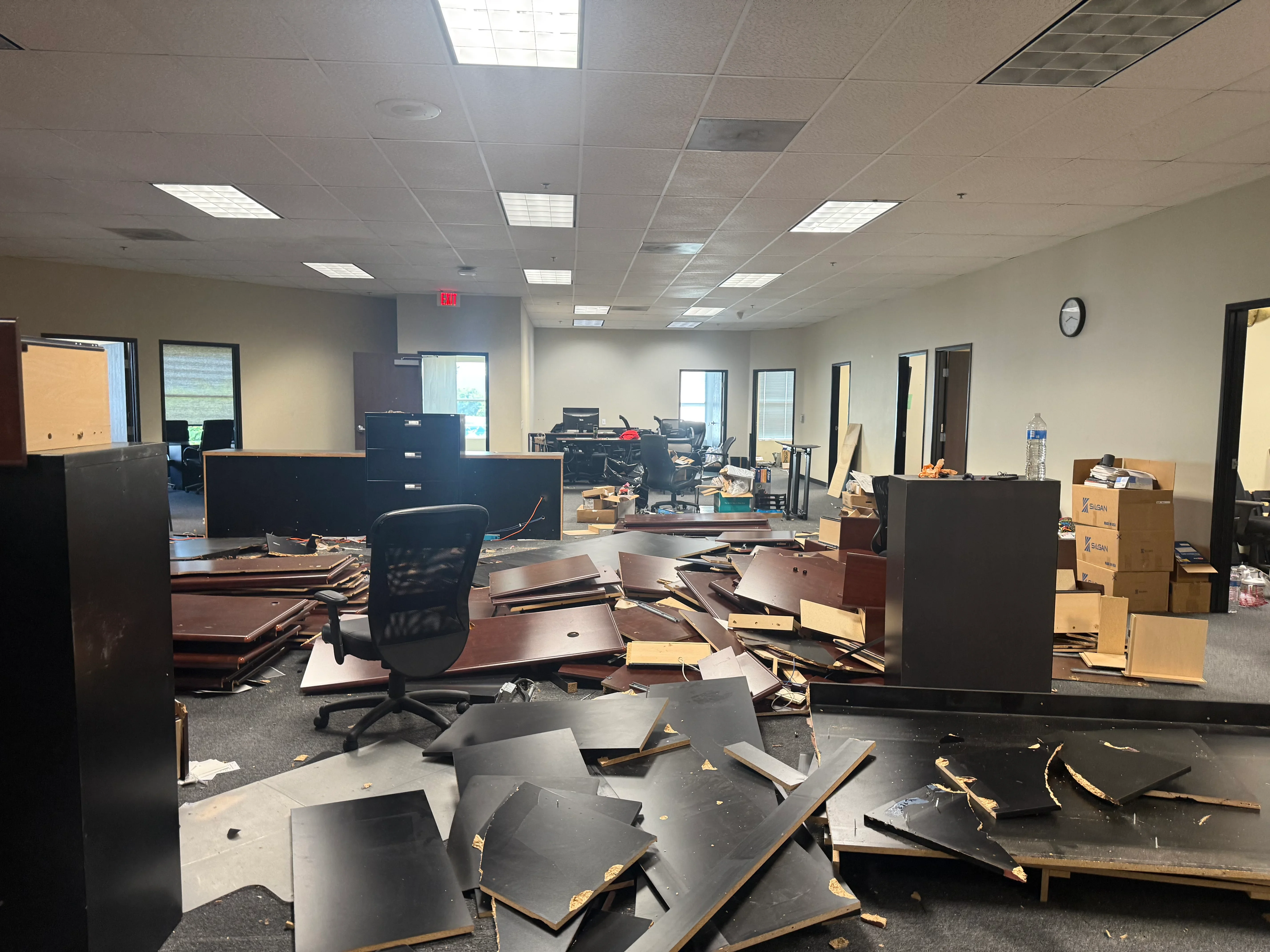 Commercial office interior with demolished furniture, metal desks, and cardboard boxes scattered across floor